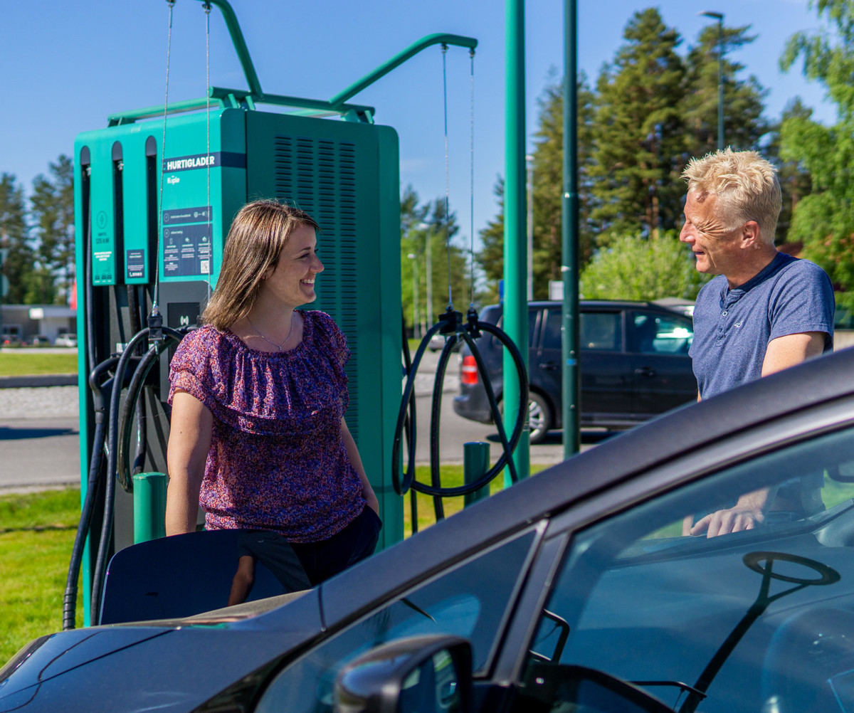 Two individuals standing in front of a charging station, wearing smiles of happiness