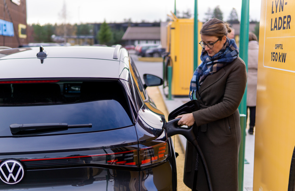 vinne i vinterklær lader en svart Volkswagen elbil ved en gul lynladestasjon